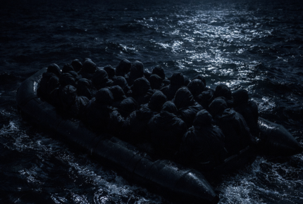 Overcrowded inflatable boat on dark water at night representing illegal immigration and the legal process following arrest for assisting illegal entry or harbouring persons in the UK